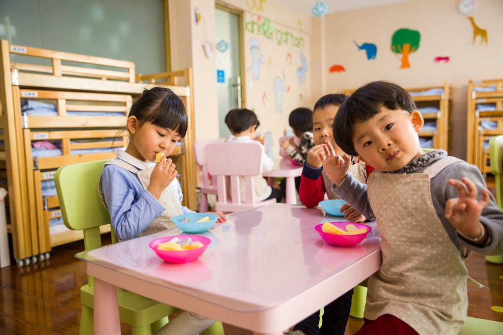 Photo by Naomi Shi Kids seated around a table in a colorful classroom, eating snacks happily.